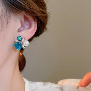 Close-up of elegant earring with emerald gemstone, blue crystal, and white pearl inlay