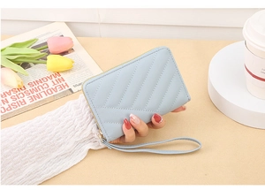 Close-up of light blue quilted wallet with wrist strap held against a lifestyle background