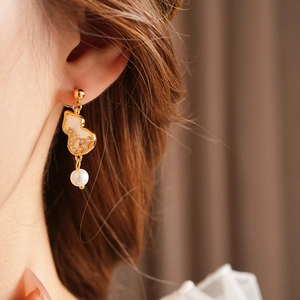 Close-up of gold gourd earrings with white stones and pearl drops on a model