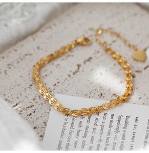 Dettaglio di un bracciale intrecciato dorato con ciondolo a cuore e catena a maglie regolabile