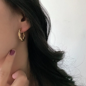 Close-up of model wearing gold-tone twisted hoop earrings with a textured metal finish