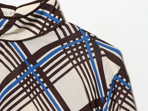 Gros plan d'un col montant à carreaux avec bouton blanc sur un tissu marron et bleu