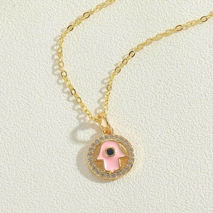 Detail of Hamsa Hand pendant with pink enamel and blue gemstone on a gold necklace