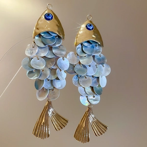 Detailed view of iridescent shell fish earrings with gold accents and blue evil eye beads
