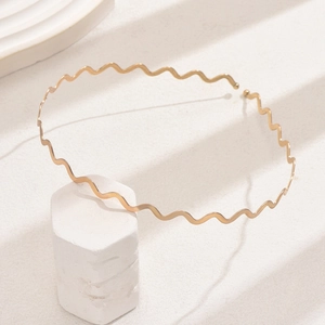 Detail of a wavy golden metal headband on a white hexagonal stone base with natural light shadow