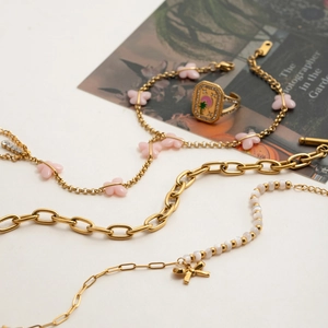 Flat lay of gold chain necklaces with pink butterfly, pearls, and palm tree signet ring