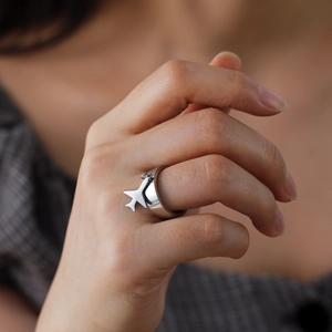Close-up of a wide stainless steel band ring featuring a delicate airplane charm