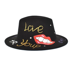 Close-up of black fedora featuring artistic graffiti red lips and gold love lettering