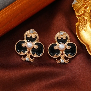 Close-up of golden clover collar pins with black enamel and pearls on dark satin fabric