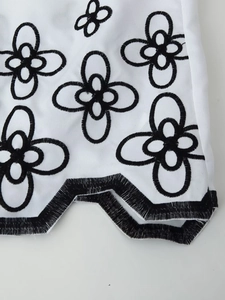 Detail of black floral embroidery and wavy hemline on a white resort-style shirt