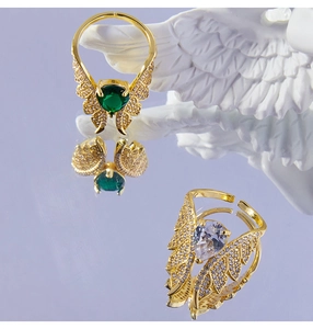 Detail of gold wing rings with green heart and white teardrop zircons on a mirror