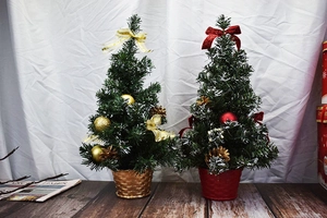 Close-up of mini Christmas trees with red and gold ornaments, pine cones and snow tips