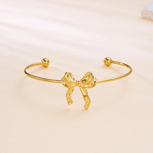 Close-up of polished gold bow-tie open bangle with spherical ends and hollow geometric pattern
