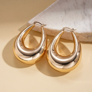 Detail of gold hollow teardrop earrings on marble display with natural lighting effects