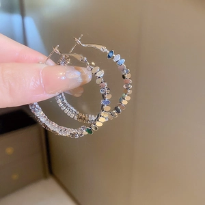 Gros plan sur des créoles argentées avec strass multicouches et détails de paillettes polies
