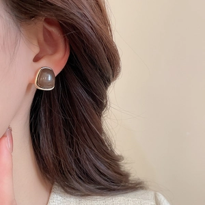 Close-up of a square grey-brown stone stud earring with vintage gold-plated metal border