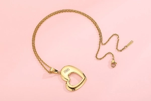 Detail of gold heart pendant with three embedded zircons on a pink background