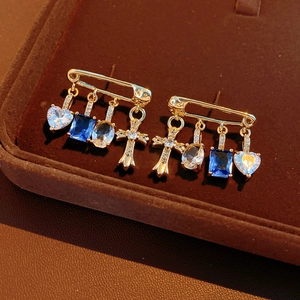 Detail of gold safety pin earrings with blue zircons, heart, and cross pendants