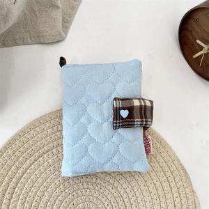 Detail of light blue quilted heart notebook cover with brown plaid strap and heart button
