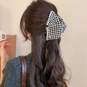 Detail of houndstooth fabric bow hair claw with pearl trim worn in a half-up hairstyle