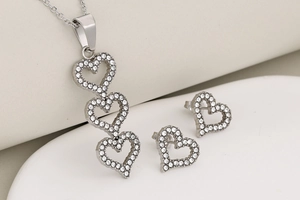 Detailed view of silver heart jewelry set with white crystals on a minimalist pedestal