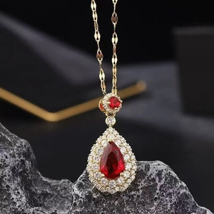 Elegant gold necklace with pear-cut red stone and sparkling white crystals on stone background