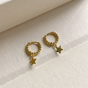 Detail view of gold beaded huggie earrings featuring polished star charms on a textured base