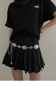 Détail de la ceinture chaîne en métal argenté vintage portée sur une jupe noire plissée