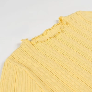 Gros plan sur un pull en maille côtelée jaune avec col montant à volants et détails