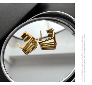 Macro shot of gold geometric square hoop earrings reflecting on a mirror surface