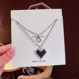 Gros plan d'un collier argenté double couche avec pendentif cœur pixel noir sur carte