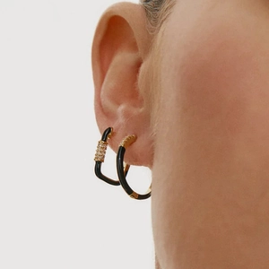 Macro side view of black enamel and gold earrings with cubic zirconia on model