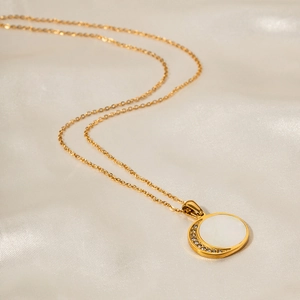 Detail of 18K gold stainless steel necklace with shell and moon pendant on silk