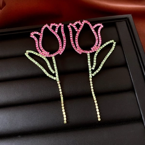 Detailed view of pink and green tulip drop earrings with rhinestones on black leather tray