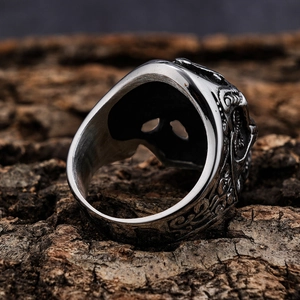 Close-up of a gothic skull ring with matte silver finish resting on a dark wood bark