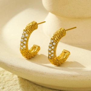 Close-up of gold geometric C-shaped earrings featuring textured relief and zircon inlay