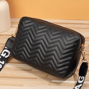 Close-up of black V-quilted leather camera bag with wide lettered strap and gold hardware