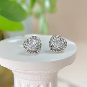 Close-up of heart-shaped silver earrings with sparkling cubic zirconia on a white stand
