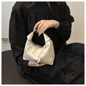 Close-up of beige silk bucket bag with floral embroidery and pearl charm detail