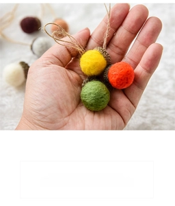 Close-up of handmade wool felt acorns with natural caps and twine loops held in hand