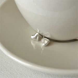 Detail of matte brushed silver heart studs leaning against a white ceramic cup edge