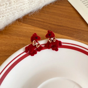 Close-up of red flocked horse earrings with pearls displayed on a white porcelain plate