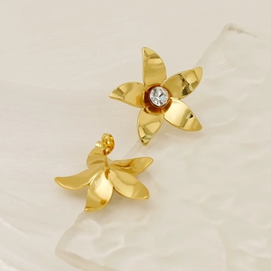 Macro view of 18k gold plated flower earrings with crystal center on a textured surface