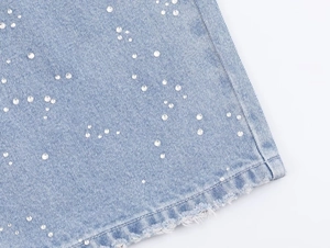 Détail de l'ourlet en jean bleu clair avec rivets en strass argentés et bords effilochés