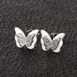 Macro shot of 3D layered butterfly stud earrings with hammered metal and white enamel