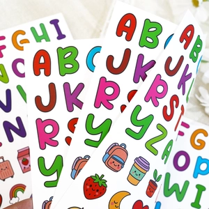 Macro shot of colorful cartoon alphabet stickers with cute hand-drawn icons on beige fabric