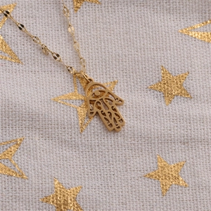 Detailed view of a gold Hamsa Hand pendant with Evil Eye on a textured star background