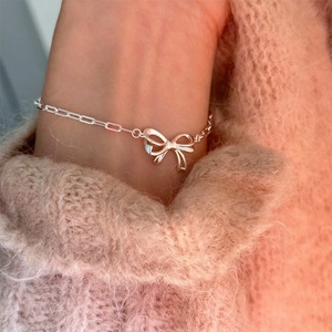 Detail of silver S925 bowknot hollow chain bracelet worn on a warm cozy sweater
