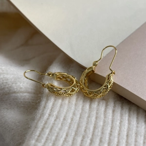 Close-up of gold hollow woven earrings showcasing intricate vintage textures on fabric
