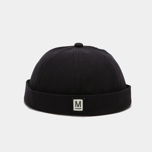 Close-up of black cotton brimless docker hat featuring a white M FASHION woven patch label